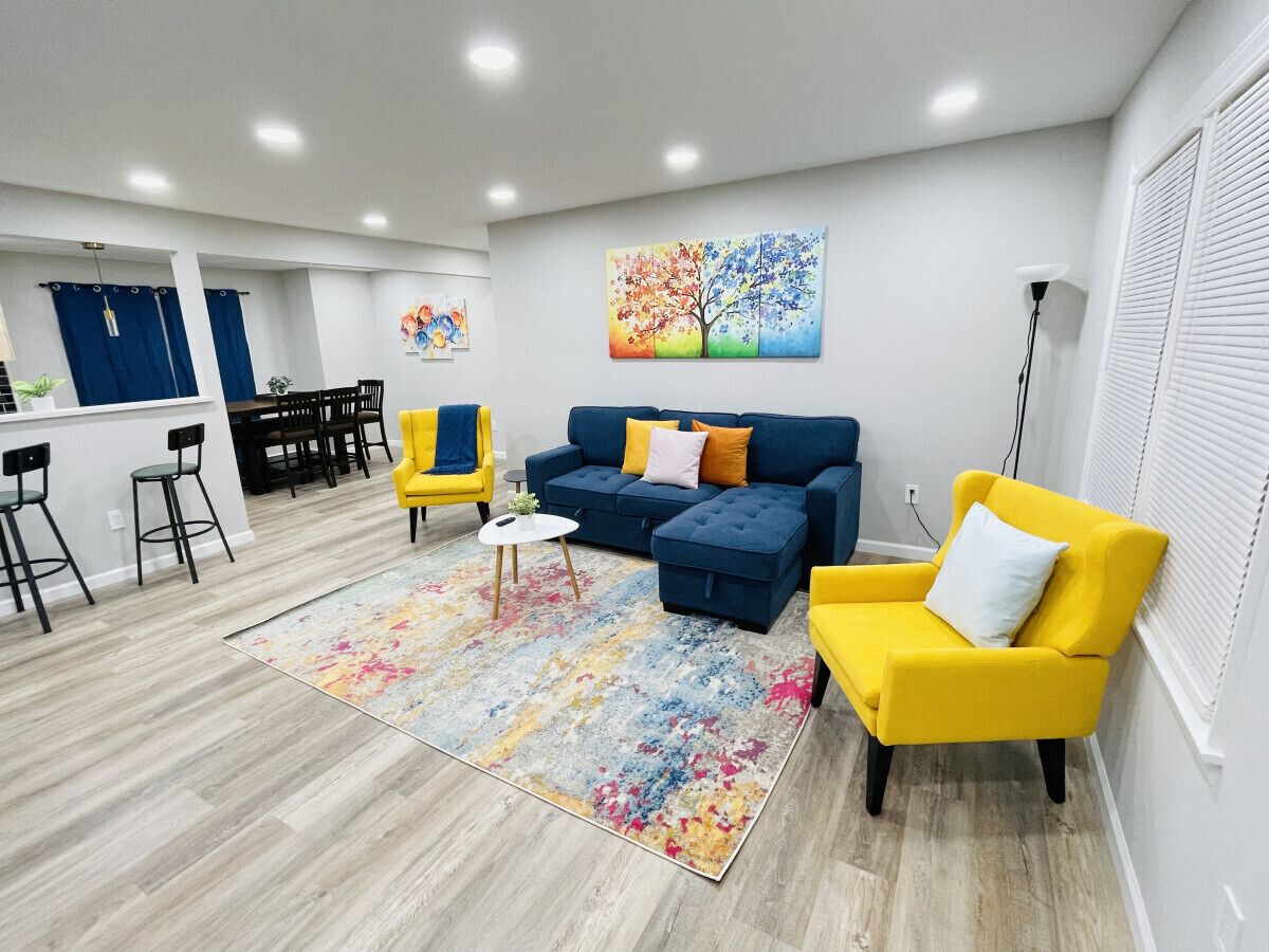 Een moderne woonkamer met een hoekbank, gele fauteuils, een salontafel en een kleurrijk vloerkleed.