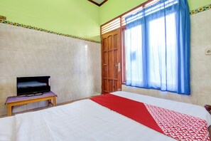 Une chambre d’hôtel avec un lit, un téléviseur posé sur une petite table et une fenêtre avec des rideaux.