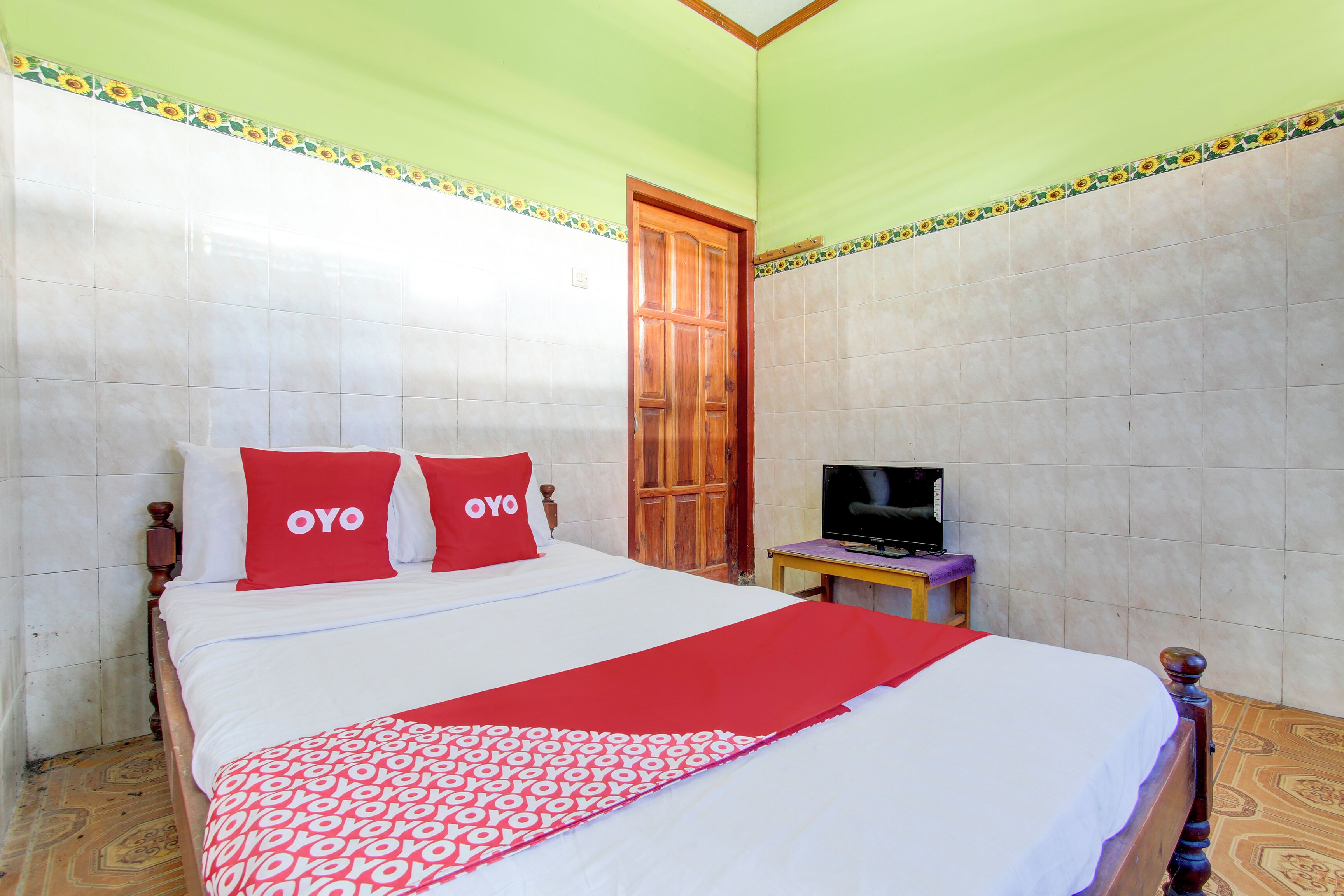 Una habitación de hotel con una cama, un televisor sobre una mesita y una puerta.