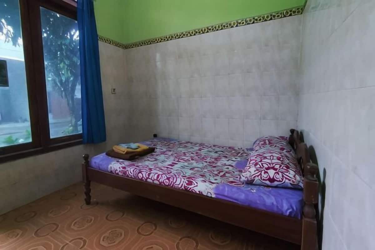 Una cama individual con una colcha y almohadas estampadas, una ventana con cortinas azules y un suelo con diseño.
