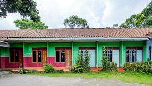 Un bâtiment à deux étages, avec un toit recouvert de tuiles, des murs verts et rouges, et des portes numérotées.