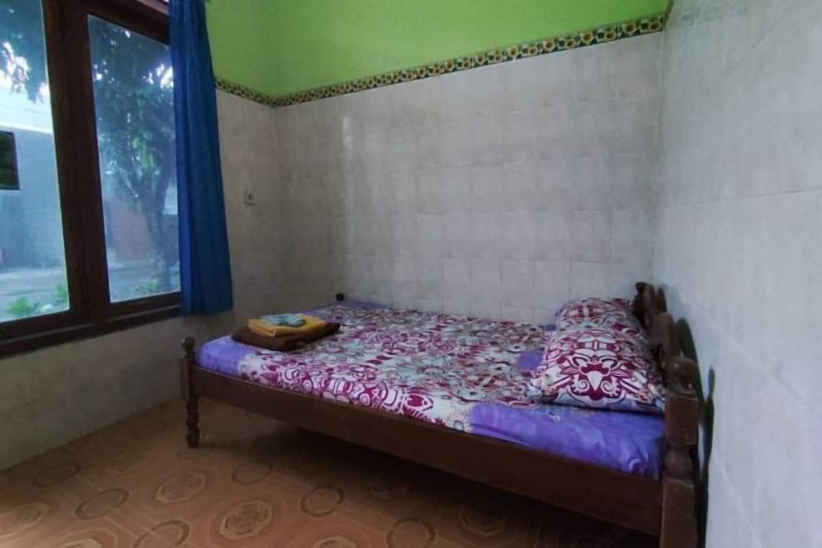 Una cama individual con una colcha estampada, una mesita de noche pequeña y una ventana con cortinas.
