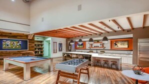 Uma sala de estar moderna com mesa de bilhar, mesa de pebolim e área de cozinha com banquetas.