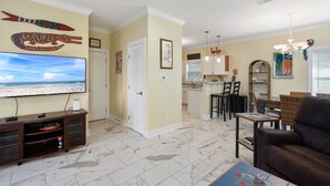 Una sala de estar con televisor, un sofá de cuero marrón y un comedor con mesa y sillas.