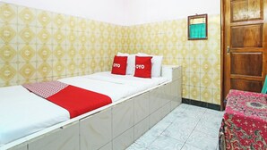 Un lit simple avec une couvre-lit rouge et blanche, deux oreillers ornés du mot « YOYO », une porte en bois et des murs à motifs.
