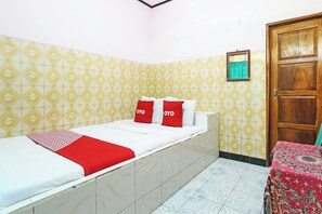 A single bed with a red and white bedspread, two pillows with the word 'YOYO' on them, a wooden door, and patterned walls. - Hotel O Pondok Wisata Sri MulyoNearSultan Agung Stadium Bantul (Cangkringan)