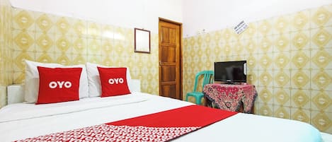 A hotel room with a bed, two red pillows, a red and white patterned bedspread, a television on a table, and a door.