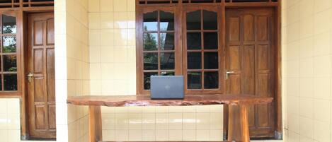 A wooden table with a laptop in front of a building with tiled walls and wooden doors.