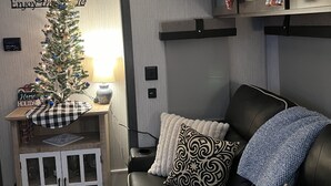 A cozy living room with a black leather sofa, a small wooden cabinet, and a Christmas tree. - Cozy camper in Clemson Hills.  5 minutes from Clemson University.  Pet friendly! (Seneca)