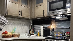 A kitchen with wooden cabinets, a microwave, an oven, and a sink. There are baskets of fruits and vegetables on the counter. - Cozy camper in Clemson Hills.  5 minutes from Clemson University.  Pet friendly! (Seneca)