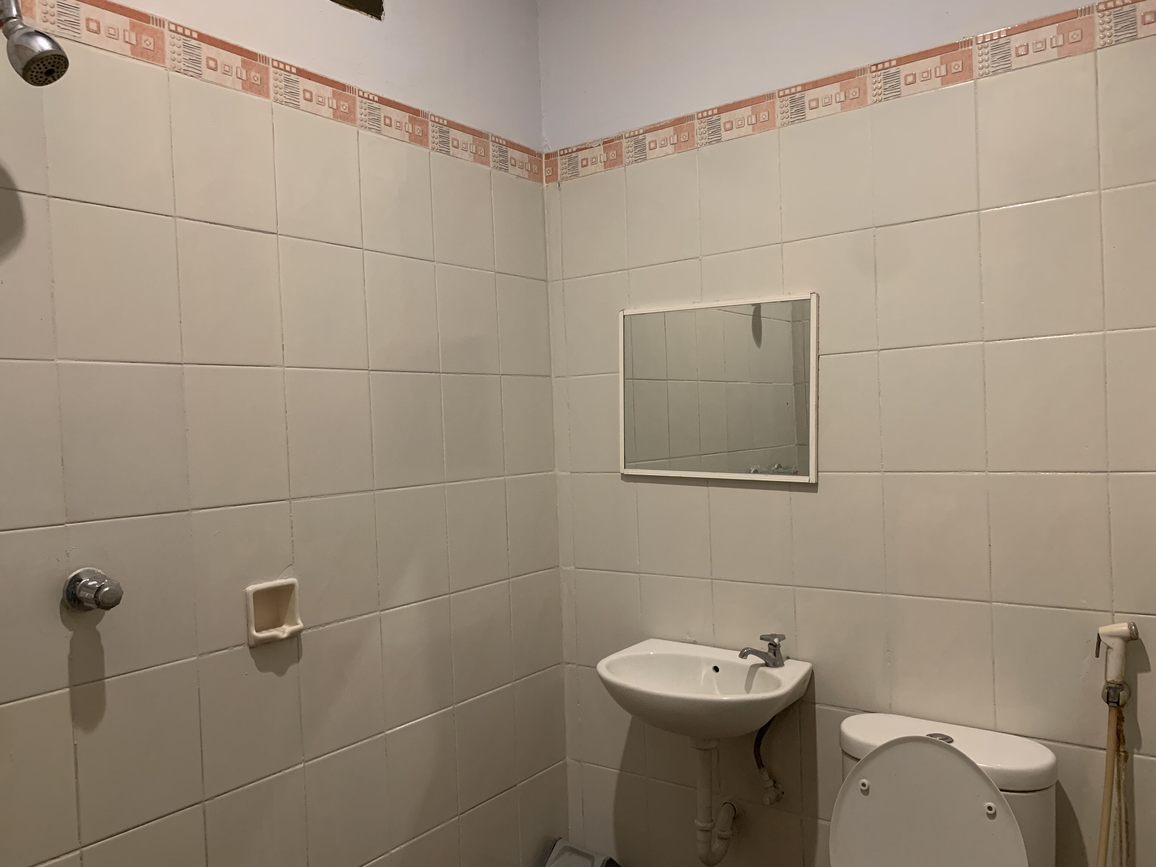 Une petite salle de bain carrelée, équipée d’un lavabo, de toilettes et d’une douche.