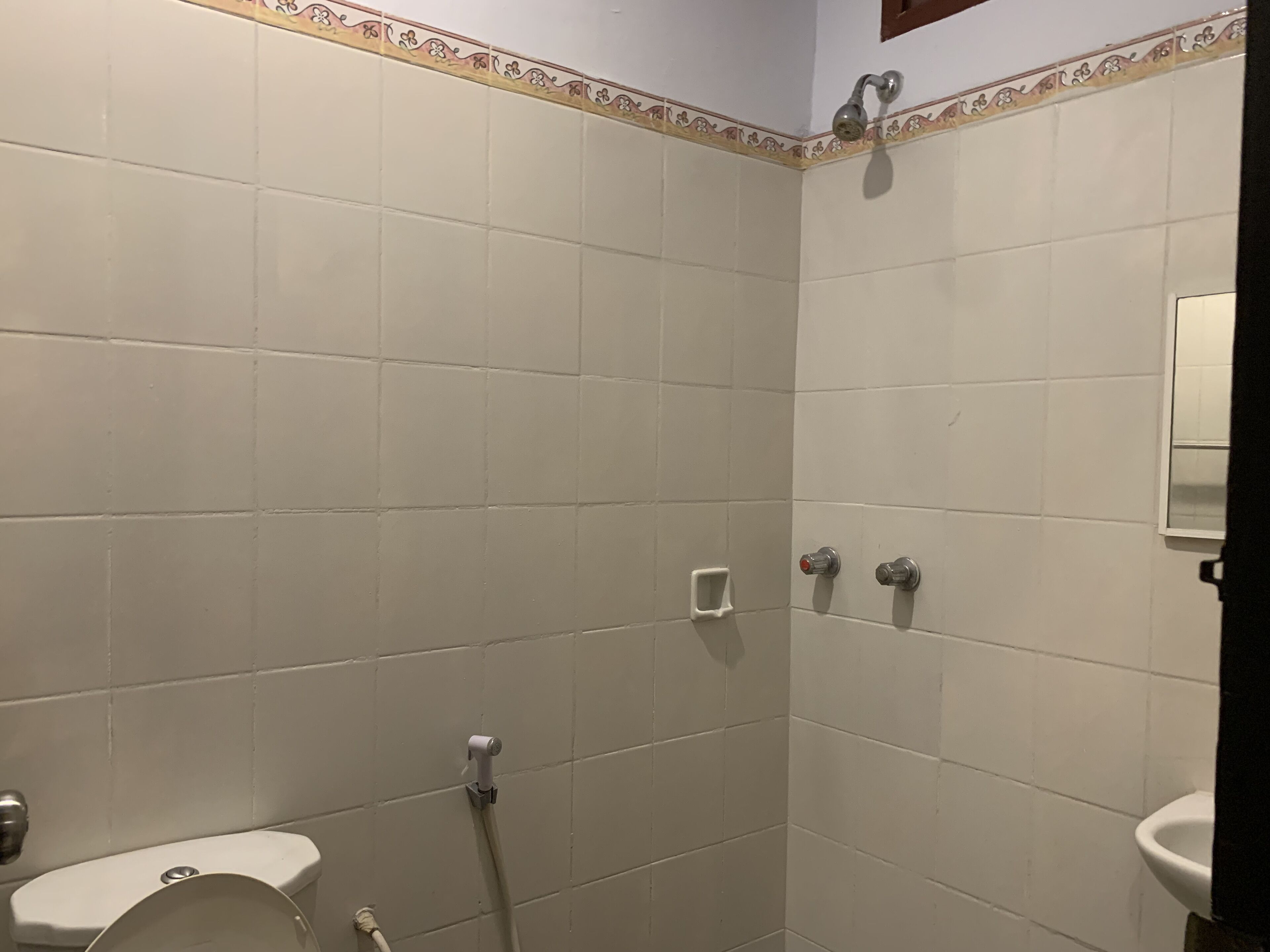 A bathroom with white tiles, a toilet, a shower, and a sink.