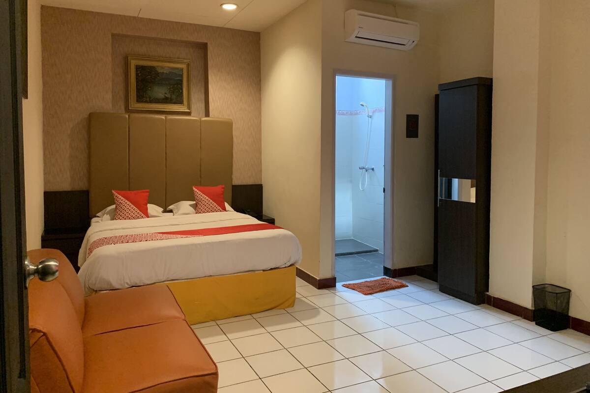 A hotel room with a bed, a sofa, a wardrobe, and an air conditioning unit.