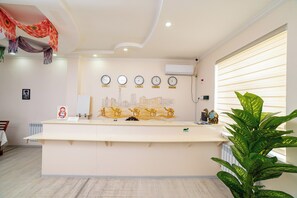 A reception desk with a cityscape mural, clocks, and a large green plant. - Caravan Boutique Inn (Khiva)