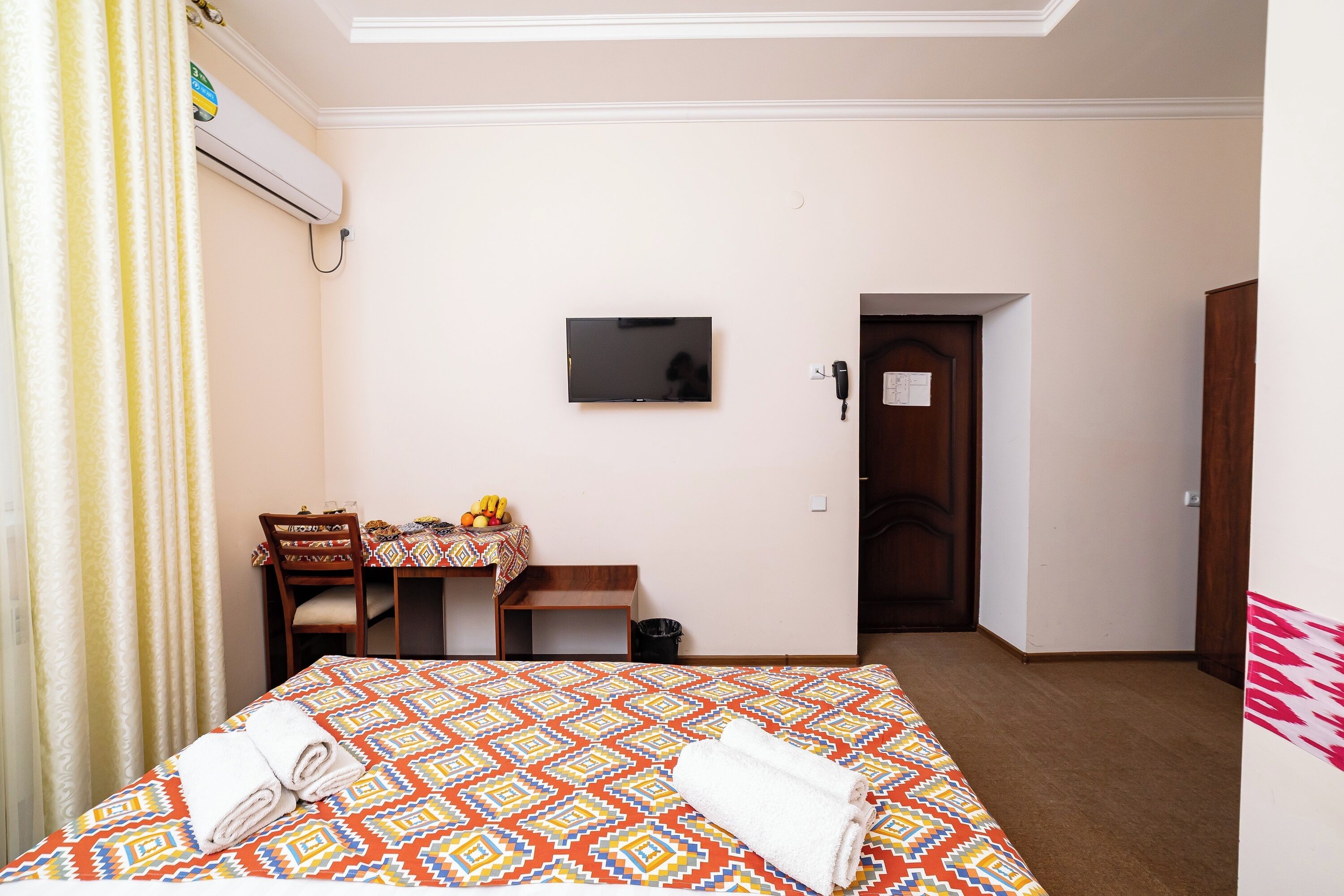 A hotel room with a bed, a desk with a chair, a television, and a door.