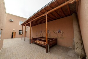 A courtyard with a bed, a covered seating area, and a wall with camel and horse paintings. - Caravan Boutique Inn (Khiva)