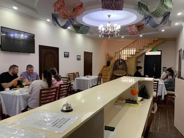 A restaurant with a long counter, multiple tables, and a staircase leading to an upper level. - Caravan Boutique Inn (Khiva)