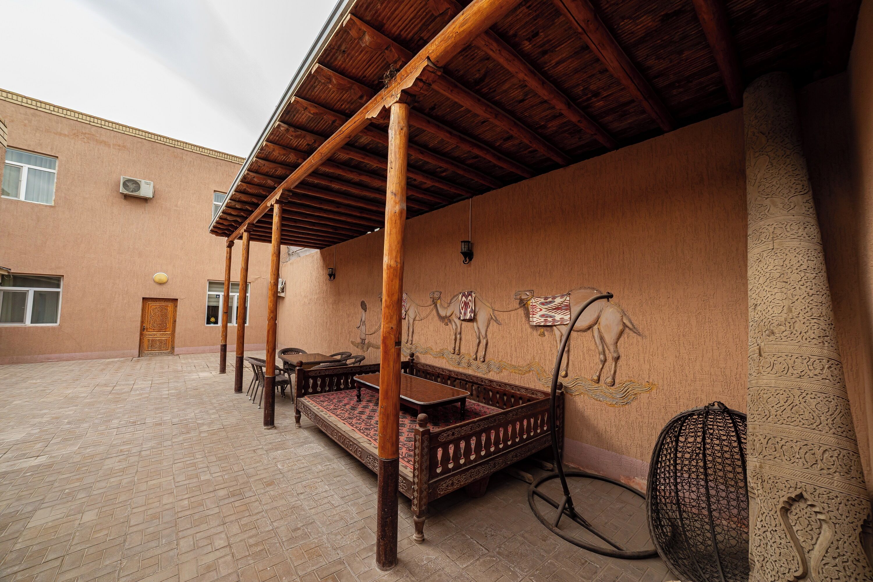 A courtyard with a wooden bench, a patterned rug, and a camel mural on the wall.