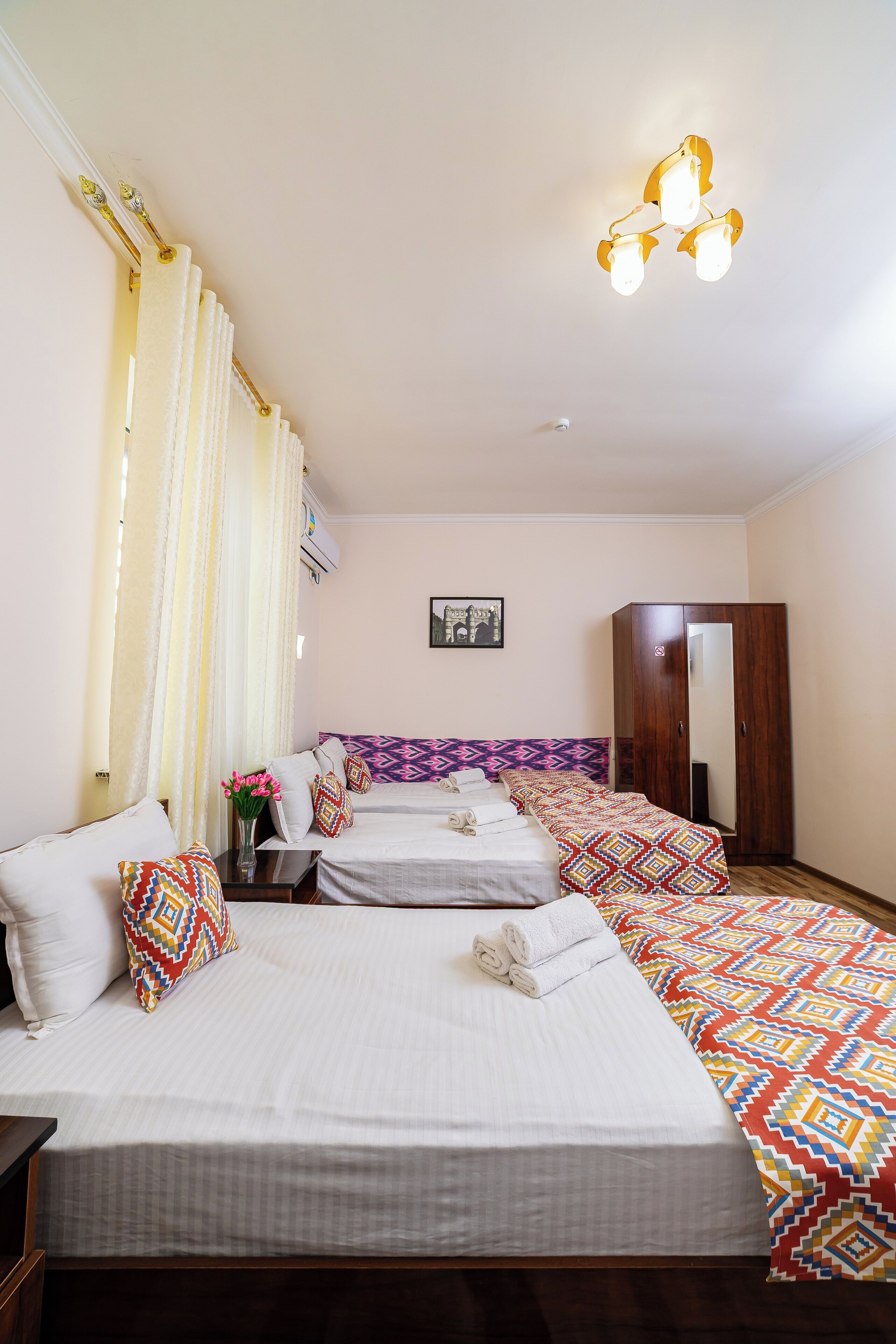 A hotel room with two beds, a wardrobe, a mirror, and a ceiling light fixture.