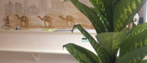 Un comptoir d’accueil orné d’horloges indiquant l’heure de différentes villes, une fresque représentant un paysage urbain et une plante en pot.