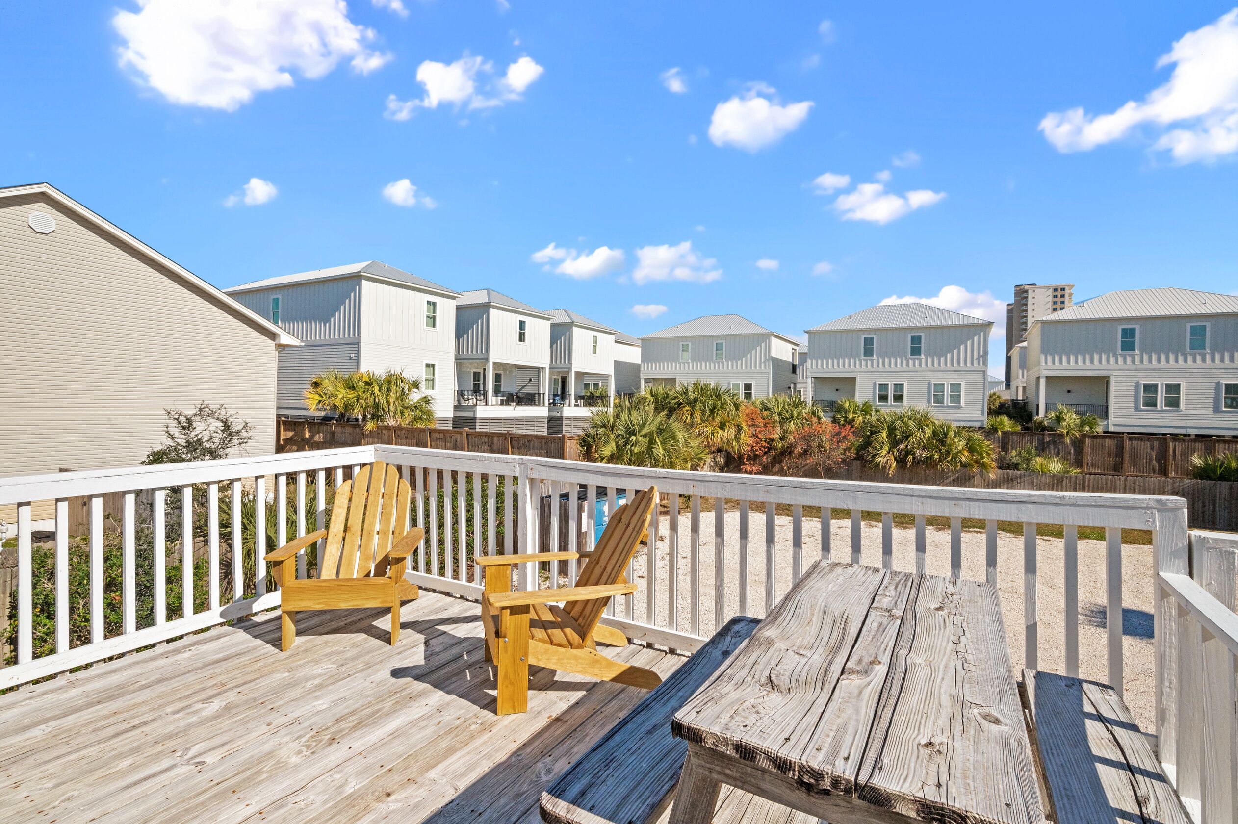 A wooden deck with two chairs and a table, overlooking a row of white houses with a clear blue sky.
