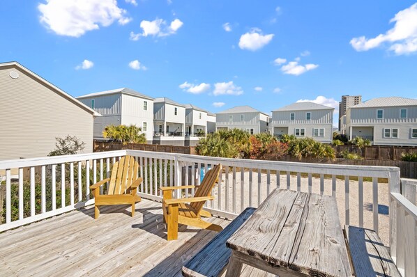 A wooden deck with two chairs and a table, overlooking a row of white houses with a clear blue sky.