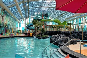 An indoor water park with a large pool, slides, and a glass ceiling.