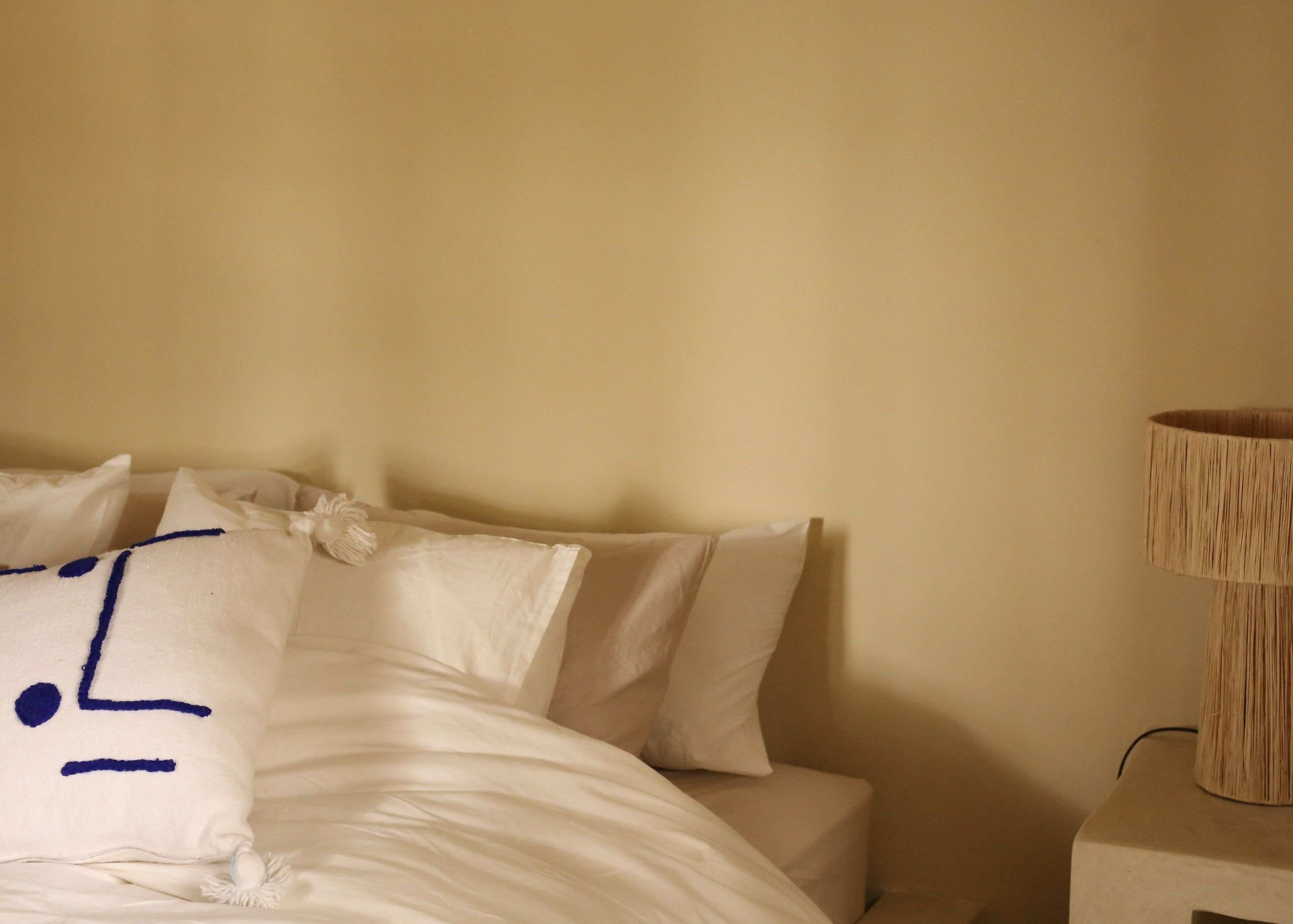 Una cama con ropa de cama blanca y un cojín decorativo con costura azul.