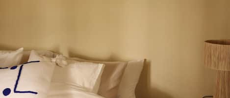 Una cama con ropa de cama blanca y un cojín decorativo con costura azul.