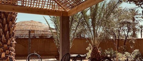 Un patio al aire libre con techo tejido, una mesa de cerámica y sillas de metal negro.