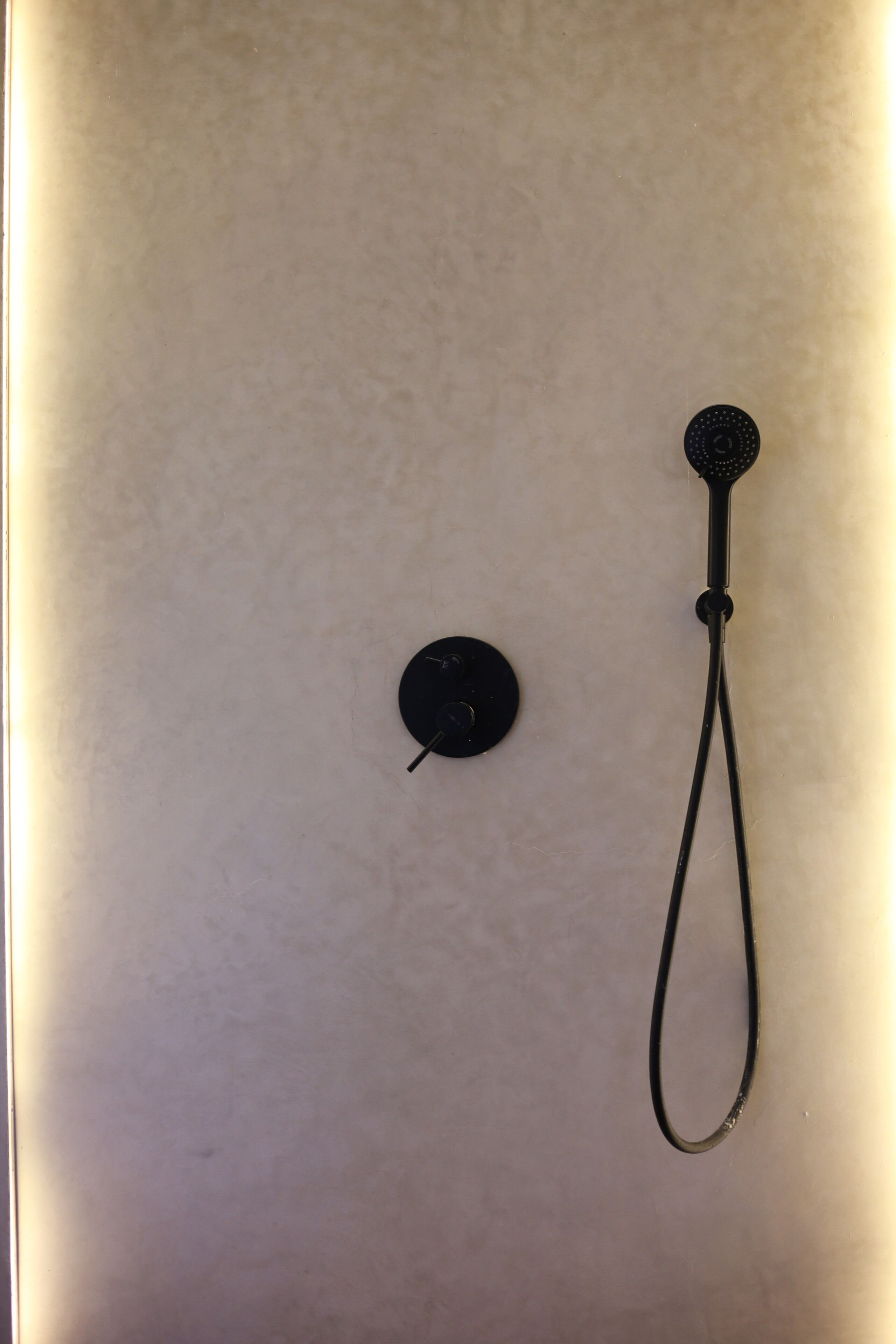 A shower with a handheld showerhead and a control knob on a plain wall.