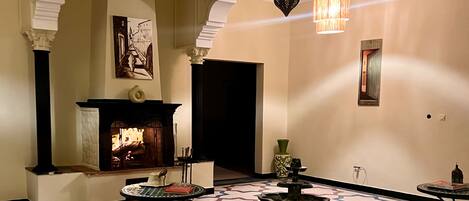 A room with a fireplace, ottomans, rugs, and a hanging light fixture.