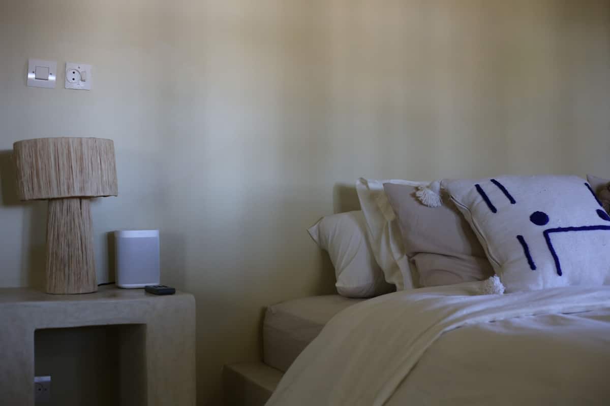 A bedroom with a bed, a bedside table with a lamp, and a power outlet on the wall.
