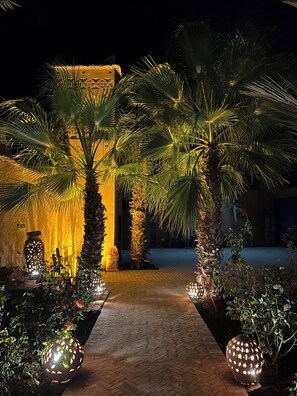 A pathway flanked by palm trees and decorative lights, leading to a building with a patterned facade. - Kasbah des Cyprès (Skoura)