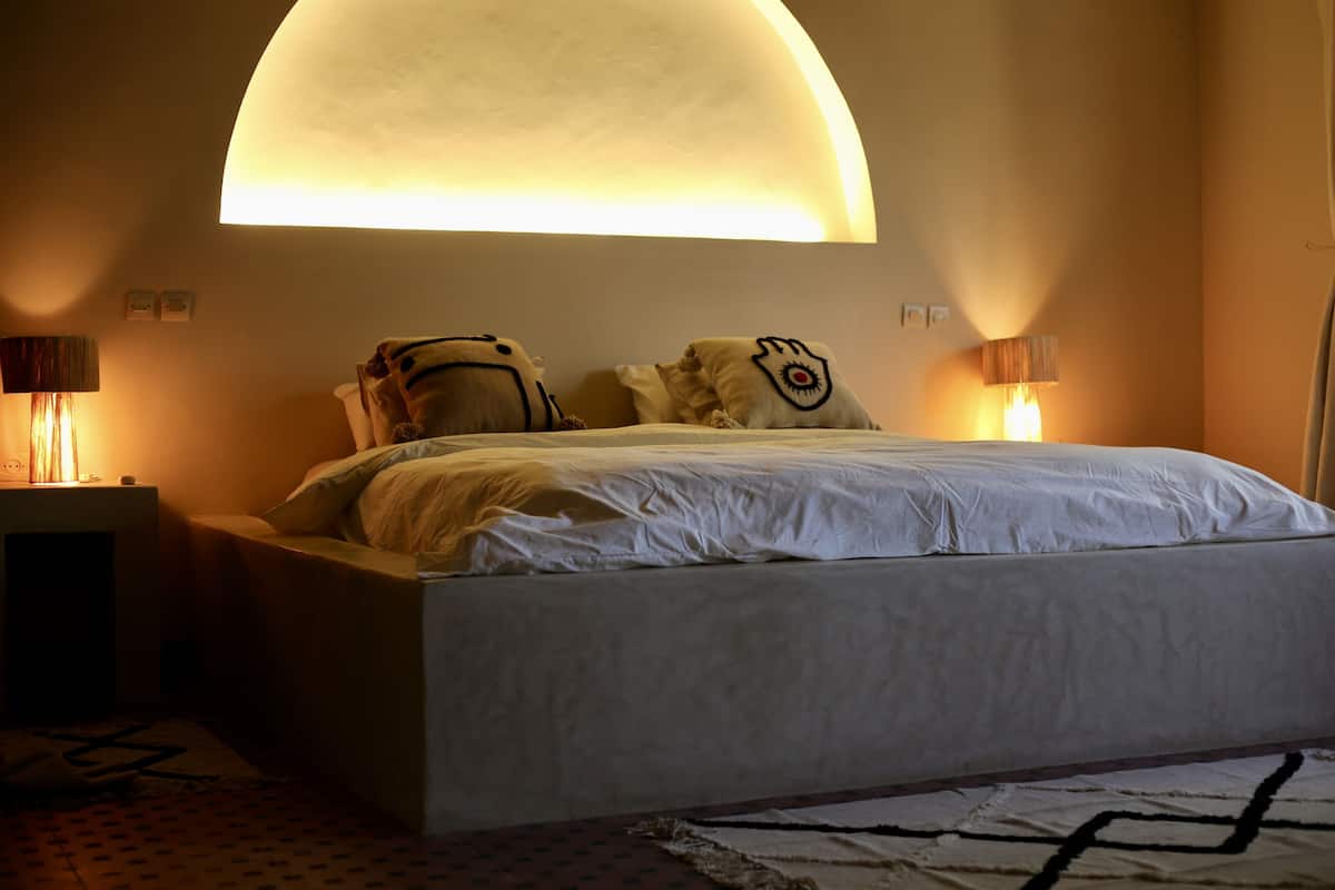 A bedroom with a large bed, two bedside lamps, a wall-mounted light fixture, and a patterned rug.