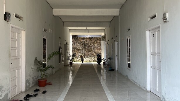 A long, narrow hallway with a tiled floor, potted plants, and numbered doors on either side. - Hotel O Pondok Bulo Ugi Syariah Near SD Negeri 185 Pinrang (Binanga Karaeng)