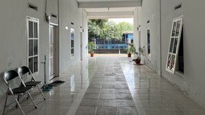A corridor with white walls, tiled floor, and doors leading to rooms. There are two chairs and potted plants along the walls. - Hotel O Pondok Bulo Ugi Syariah Near SD Negeri 185 Pinrang (Binanga Karaeng)