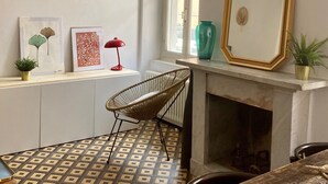 Una habitación con chimenea, una silla, un ventanal y obras de arte en la pared.