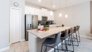 A modern kitchen with white cabinets, stainless steel appliances, and a central island with bar stools. - Family 4BR w/ Private Pool near Disney Parks! (Kissimmee)