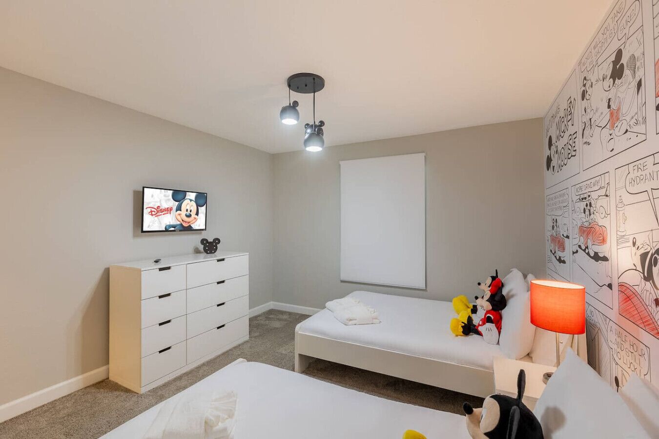 A bedroom with a bed, a dresser, a TV, and a wall with comic strip art.
