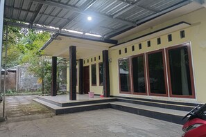 A covered outdoor area with steps leading to a building entrance, a red vehicle parked nearby, and a clear view of the surrounding greenery. - Hotel O Penginapan Annisya Near SMA Negeri 2 Mataram (Mataram)