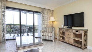 Una camera d'hotel con un balcone, una televisione, una poltrona a righe, un tavolo e una lampada.