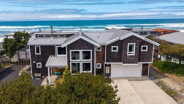 A two-story house with a garage, a covered porch, and a view of the ocean. - Stunning Home: Spacious layout, perfect for gathering with friends or family. (Rockaway Beach)