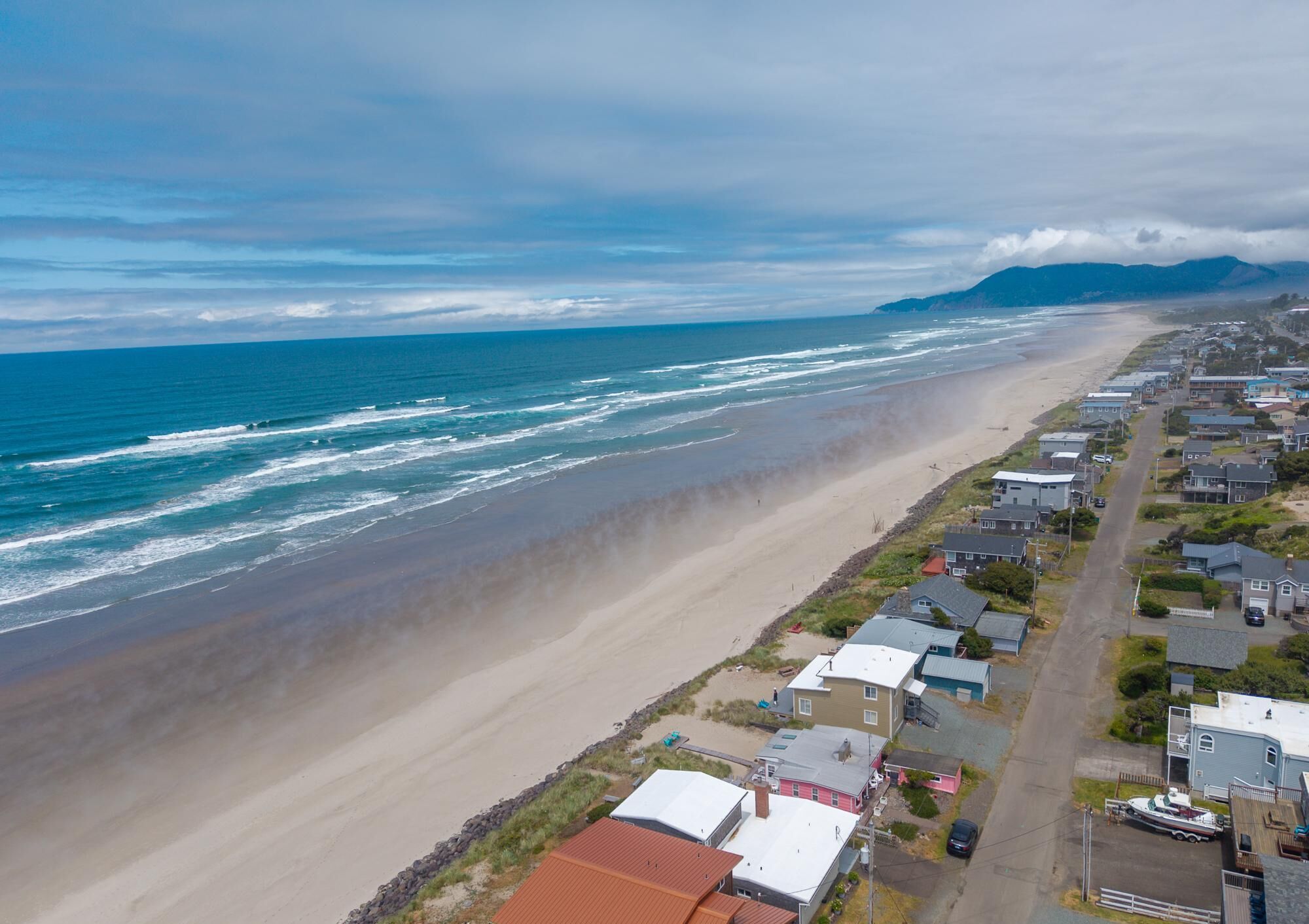 A coastal residential area with houses along the beach, a clear view of the ocean, and distant mountains.