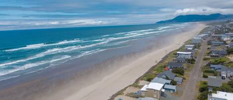 A coastal residential area with houses along the beach, a clear view of the ocean, and distant mountains.