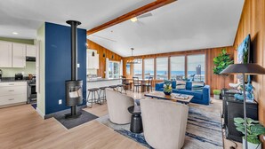 A modern living room with a large window, a fireplace, and a dining area. - Stunning Home: Spacious layout, perfect for gathering with friends or family. (Rockaway Beach)