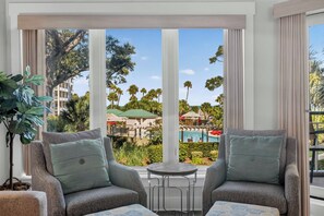 A room with two grey armchairs, a small round table, and a view of a pool and palm trees. - Oceanfront luxury, ocean and pool views, good availability 3104 Windsor Court (Hilton Head)