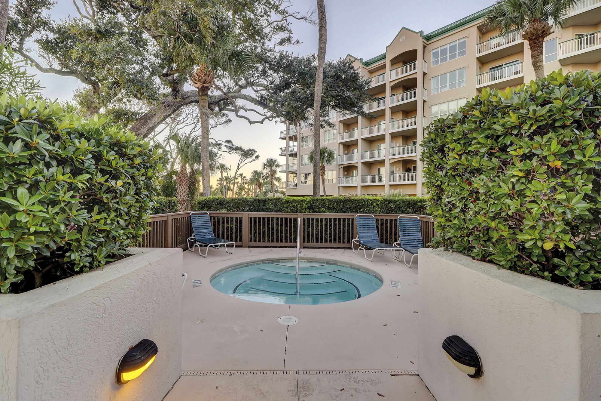 Un espace piscine avec des chaises longues, un jacuzzi et un bâtiment doté de balcons en arrière-plan.