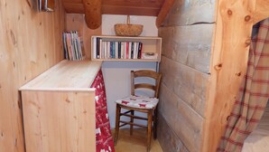 A cozy wooden cabin with a skylight, a small table with a red and white tablecloth, a chair, and a bookshelf filled with books. - Le Chalet du Papote (Aussois)