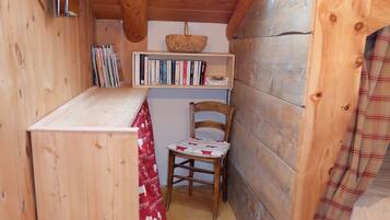 Une cabane en bois chaleureuse, dotée d’une lucarne, d’une petite table recouverte d’une nappe rouge et blanche, d’une chaise et d’une bibliothèque remplie de livres.